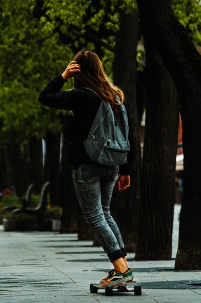 白天，一名身穿黑色皮夹克和蓝色牛仔牛仔裤的妇女站在人行道上